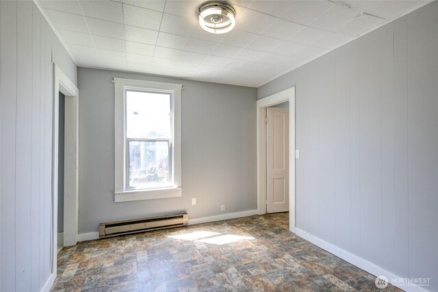 empty room with a baseboard heating unit, stone finish floors, baseboards, and wood walls