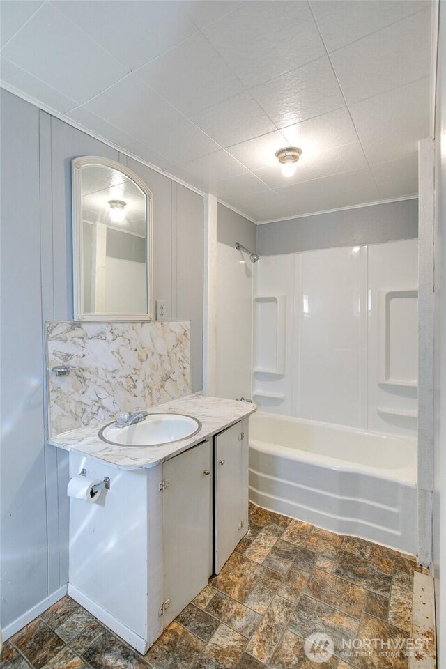 full bathroom featuring vanity, bathing tub / shower combination, stone finish floors, and a decorative wall