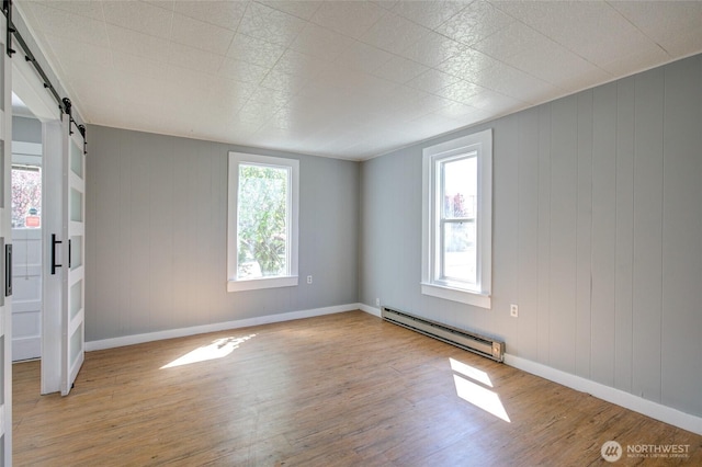 spare room featuring a barn door, baseboard heating, light wood-style floors, and baseboards