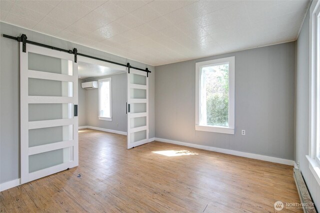 unfurnished room with a barn door, an AC wall unit, wood finished floors, and baseboards