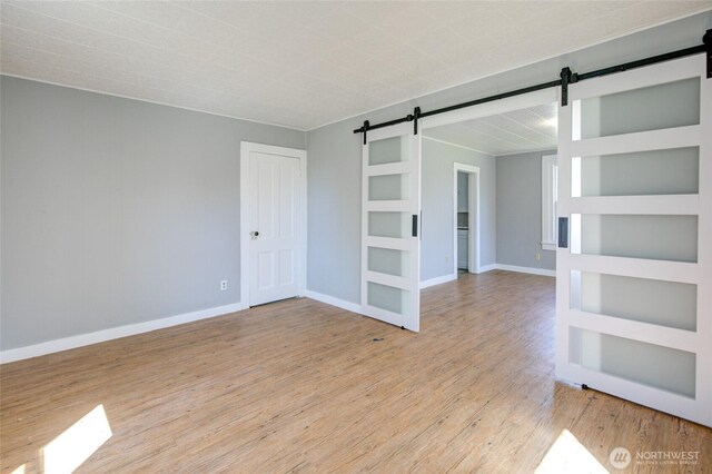 empty room featuring a barn door, light wood-style flooring, and baseboards