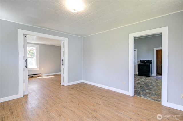 spare room featuring baseboard heating, light wood-style floors, and baseboards