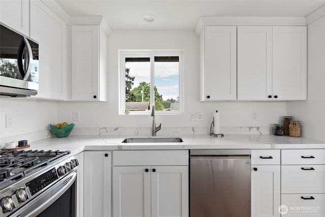 kitchen with stainless steel appliances, a sink, white cabinets, and light stone countertops