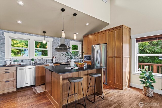 1533 S Sunset Dr, Tacoma, WA 98465 - kitchen with stainless steel appliances, wall chimney exhaust hood, dark countertops, a kitchen island, and tasteful backsplash