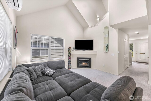 carpeted living area with high vaulted ceiling, baseboards, and a glass covered fireplace