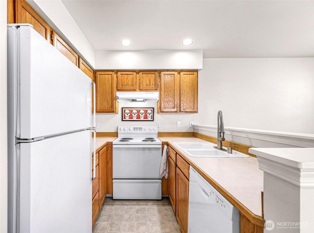 kitchen with white appliances, under cabinet range hood, a sink, brown cabinetry, and light countertops