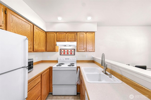kitchen featuring white appliances, under cabinet range hood, a sink, light countertops, and brown cabinets