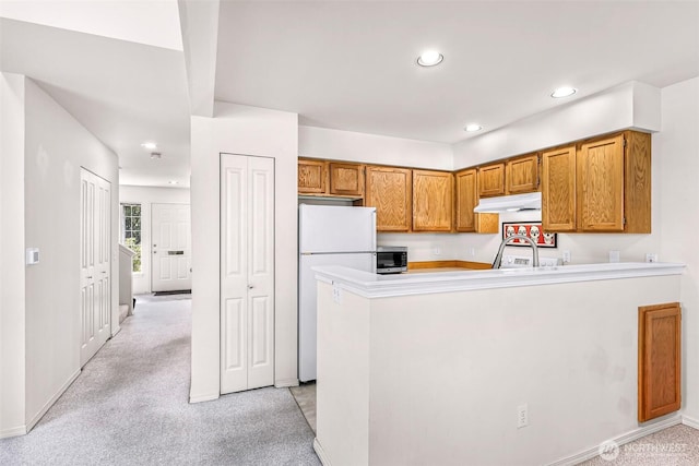 kitchen featuring under cabinet range hood, freestanding refrigerator, light colored carpet, recessed lighting, and a peninsula