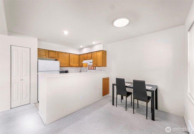 kitchen featuring freestanding refrigerator, brown cabinetry, under cabinet range hood, a peninsula, and light countertops