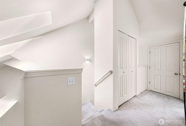 corridor with an upstairs landing, vaulted ceiling, and carpet flooring
