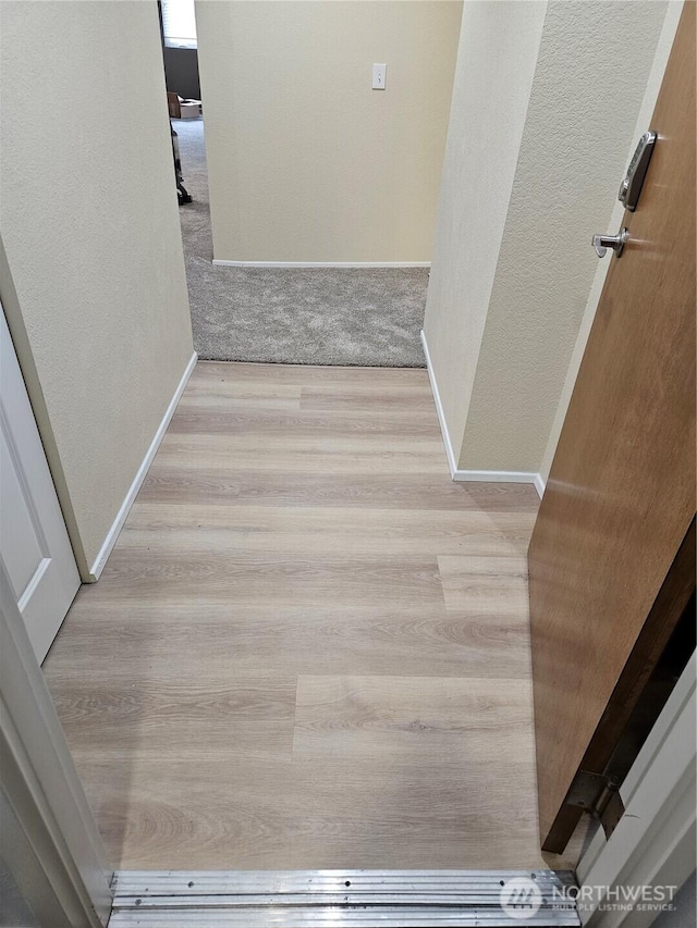 hall with wood finished floors, a textured wall, and baseboards