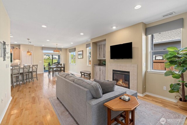 living area with light wood finished floors, a tiled fireplace, baseboards, and recessed lighting
