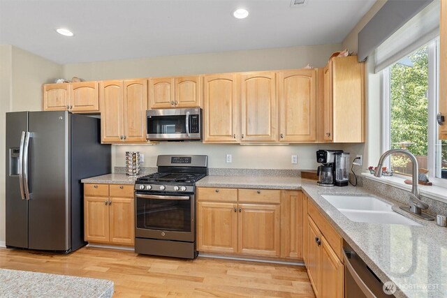 kitchen with appliances with stainless steel finishes, a sink, light brown cabinets, light wood finished floors, and recessed lighting