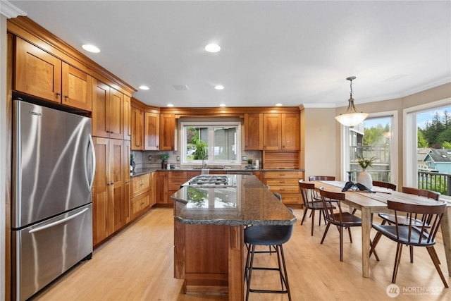 kitchen with appliances with stainless steel finishes, a sink, light wood finished floors, brown cabinets, and crown molding
