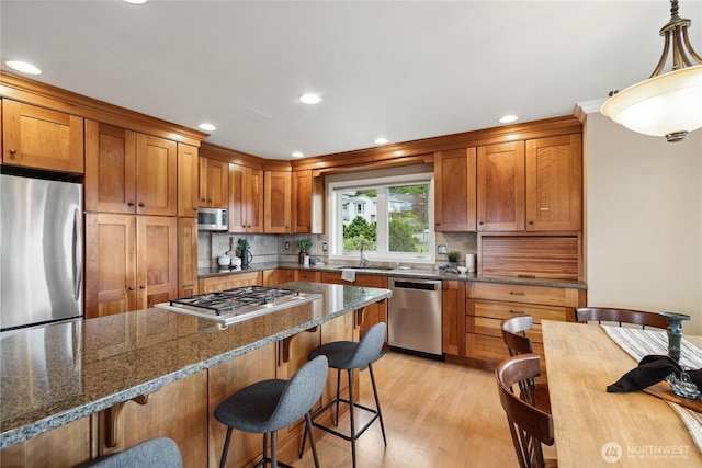 kitchen with stainless steel appliances, a sink, a breakfast bar area, light wood-style flooring, and decorative backsplash