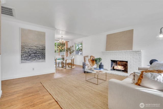 living room featuring a chandelier, light wood-style floors, crown molding, a brick fireplace, and baseboards