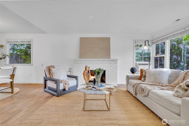 living area with wood finished floors, healthy amount of natural light, a brick fireplace, ornamental molding, and cooling unit