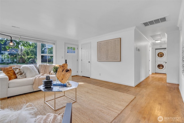 living room featuring stacked washer / drying machine, crown molding, wood finished floors, and baseboards
