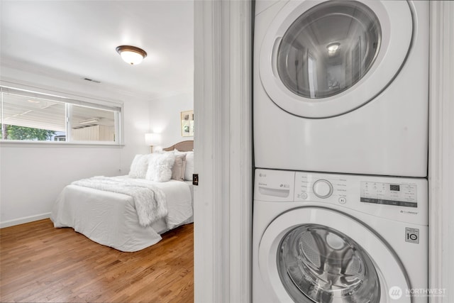 laundry area featuring stacked washing machine and dryer, wood finished floors, baseboards, and crown molding