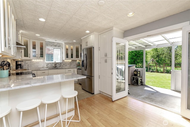 kitchen with appliances with stainless steel finishes, a peninsula, wall chimney exhaust hood, tasteful backsplash, and white cabinets