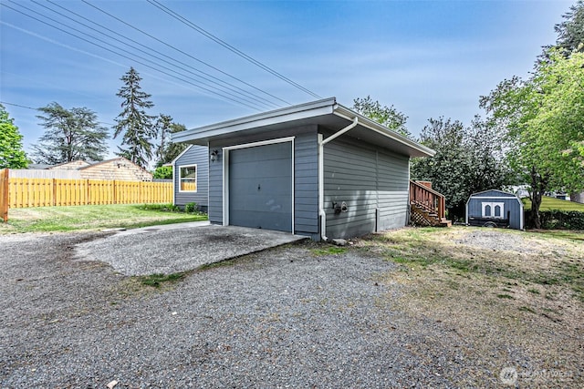 detached garage with fence, driveway, and a storage shed