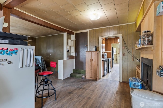 kitchen with wood walls, freestanding refrigerator, a fireplace with raised hearth, wood finished floors, and ornamental molding