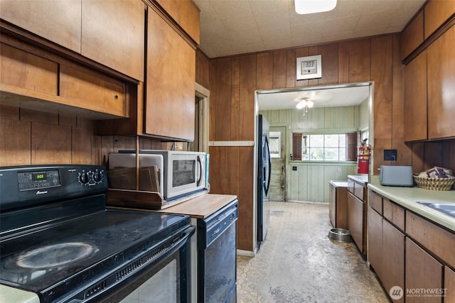 kitchen featuring black appliances, light countertops, wooden walls, brown cabinetry, and concrete floors