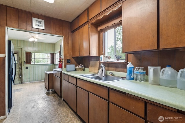 kitchen with a sink, light countertops, plenty of natural light, wood walls, and freestanding refrigerator