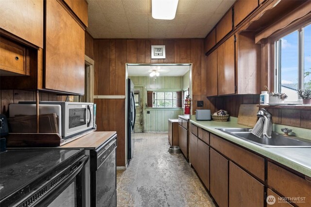 kitchen with wood walls, light countertops, a sink, electric stove, and dishwashing machine