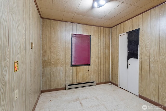 carpeted empty room featuring a baseboard radiator, wooden walls, and baseboards