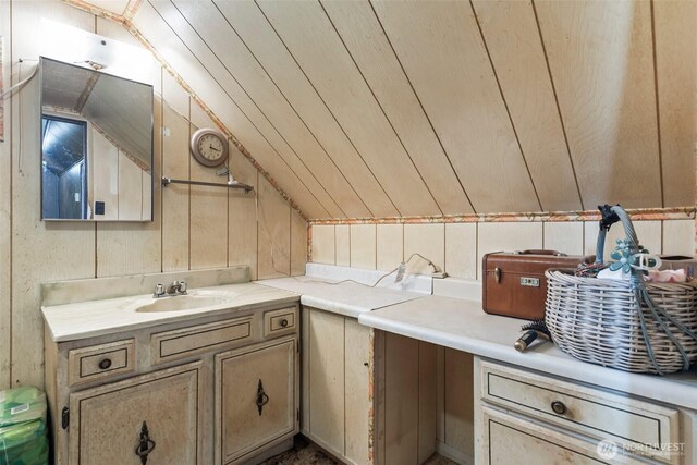 bathroom with vaulted ceiling, wooden walls, and vanity
