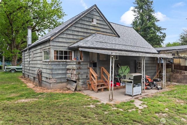 back of house with roof with shingles, a yard, and a patio area