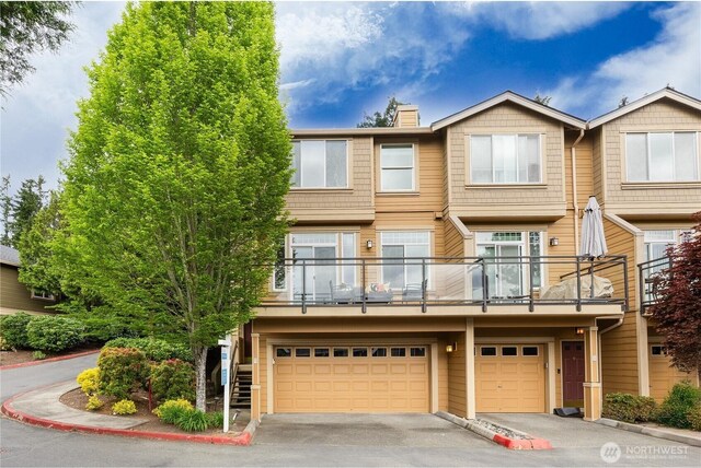 view of property featuring an attached garage, asphalt driveway, a chimney, and a balcony