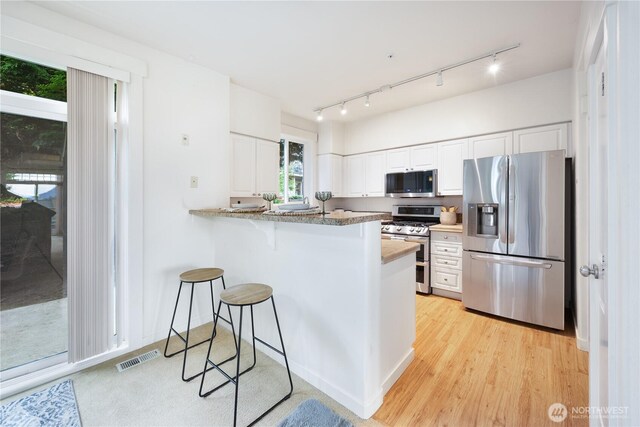 kitchen with appliances with stainless steel finishes, white cabinetry, a kitchen breakfast bar, a peninsula, and light wood finished floors