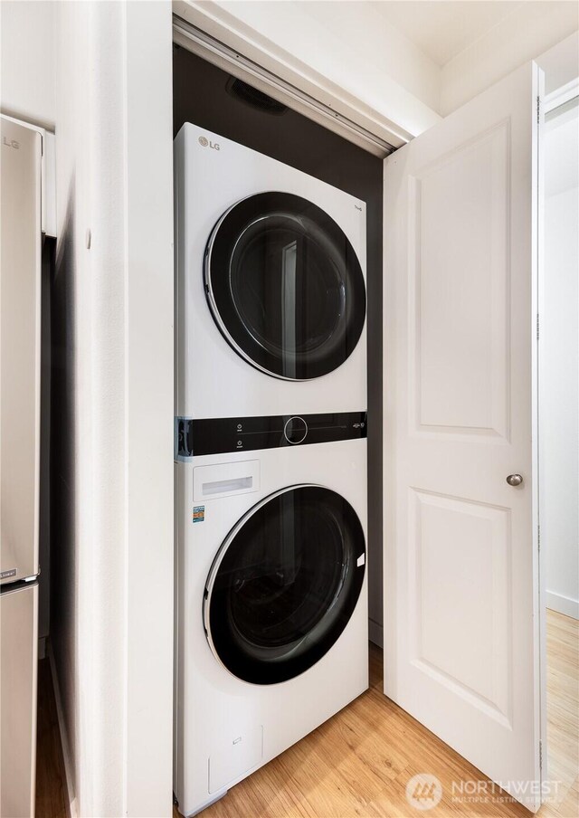 washroom with stacked washing machine and dryer and light wood finished floors