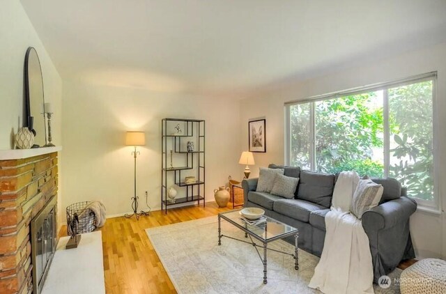 living room with a brick fireplace, light wood finished floors, and baseboards