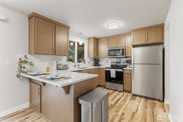 kitchen featuring stainless steel appliances, a peninsula, a sink, light wood-style flooring, and light countertops