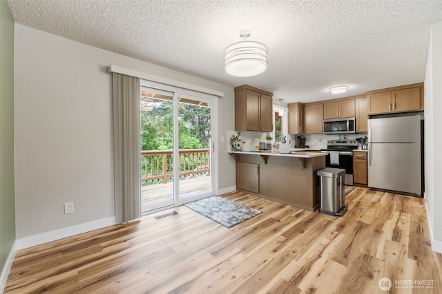 kitchen featuring stainless steel appliances, a sink, a peninsula, a textured ceiling, and light wood-style floors