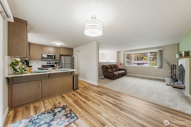 kitchen with appliances with stainless steel finishes, open floor plan, a peninsula, a textured ceiling, and light wood-style floors