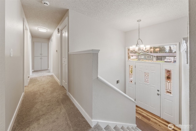 entrance foyer featuring a chandelier, a textured ceiling, light carpet, and baseboards