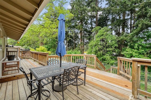 deck with outdoor dining space and view of wooded area