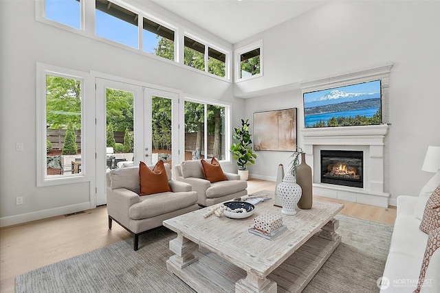 1038 Belfair Rd, Bellevue, WA 98004 - living room featuring a high ceiling, a glass covered fireplace, light wood-style flooring, baseboards, and french doors