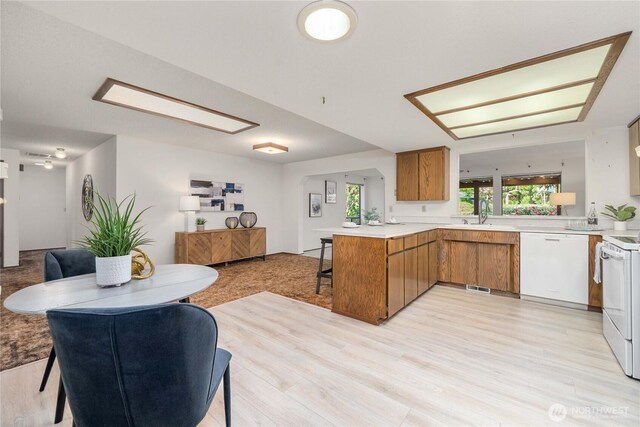 kitchen with white appliances, brown cabinets, open floor plan, a peninsula, and light countertops