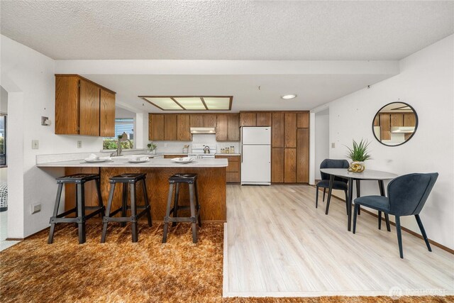 kitchen featuring freestanding refrigerator, a peninsula, light wood-style flooring, light countertops, and brown cabinets