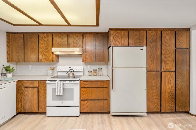 kitchen featuring white appliances, under cabinet range hood, and brown cabinetry