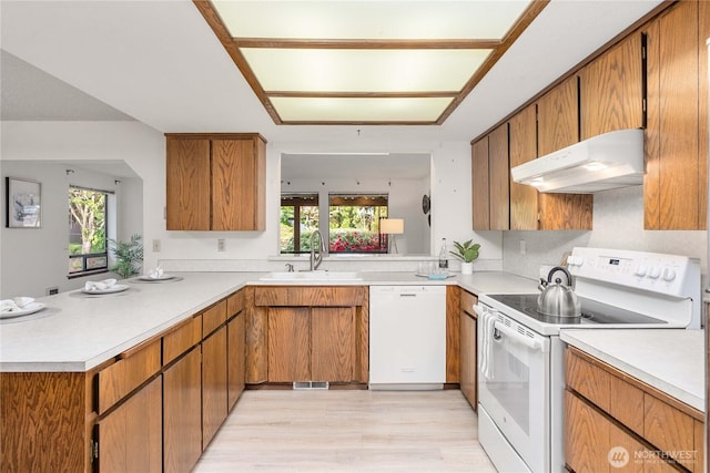 kitchen with white appliances, under cabinet range hood, a sink, and light countertops