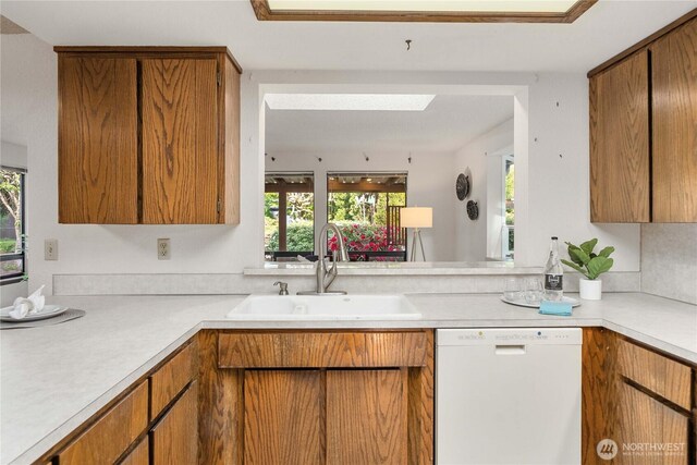 kitchen with white dishwasher, a sink, light countertops, and healthy amount of natural light
