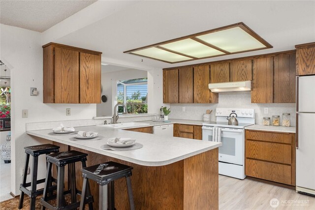 kitchen with white appliances, under cabinet range hood, a sink, light countertops, and a peninsula
