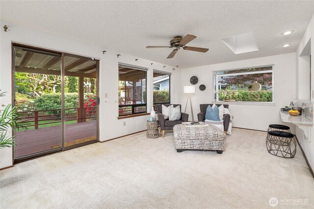 sitting room with ceiling fan, carpet floors, a textured ceiling, baseboards, and a skylight