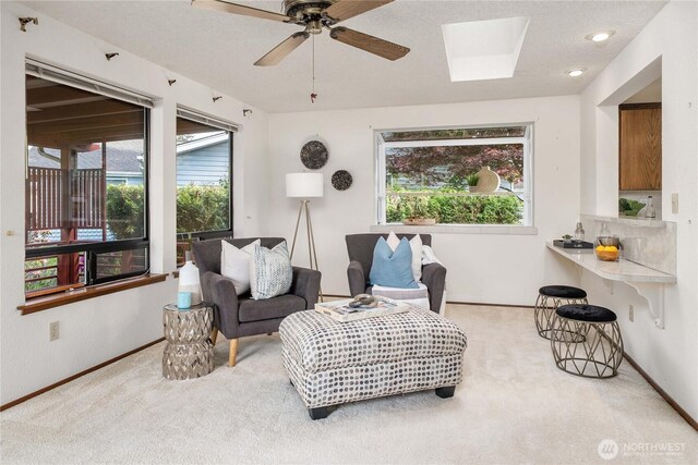 living room with carpet flooring, baseboards, a ceiling fan, and a skylight
